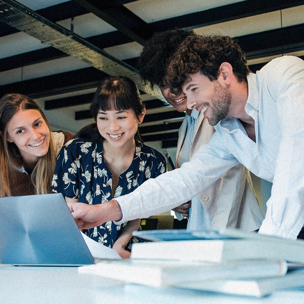 Four people looking at a laptop screen laughing while one person points at the screen
