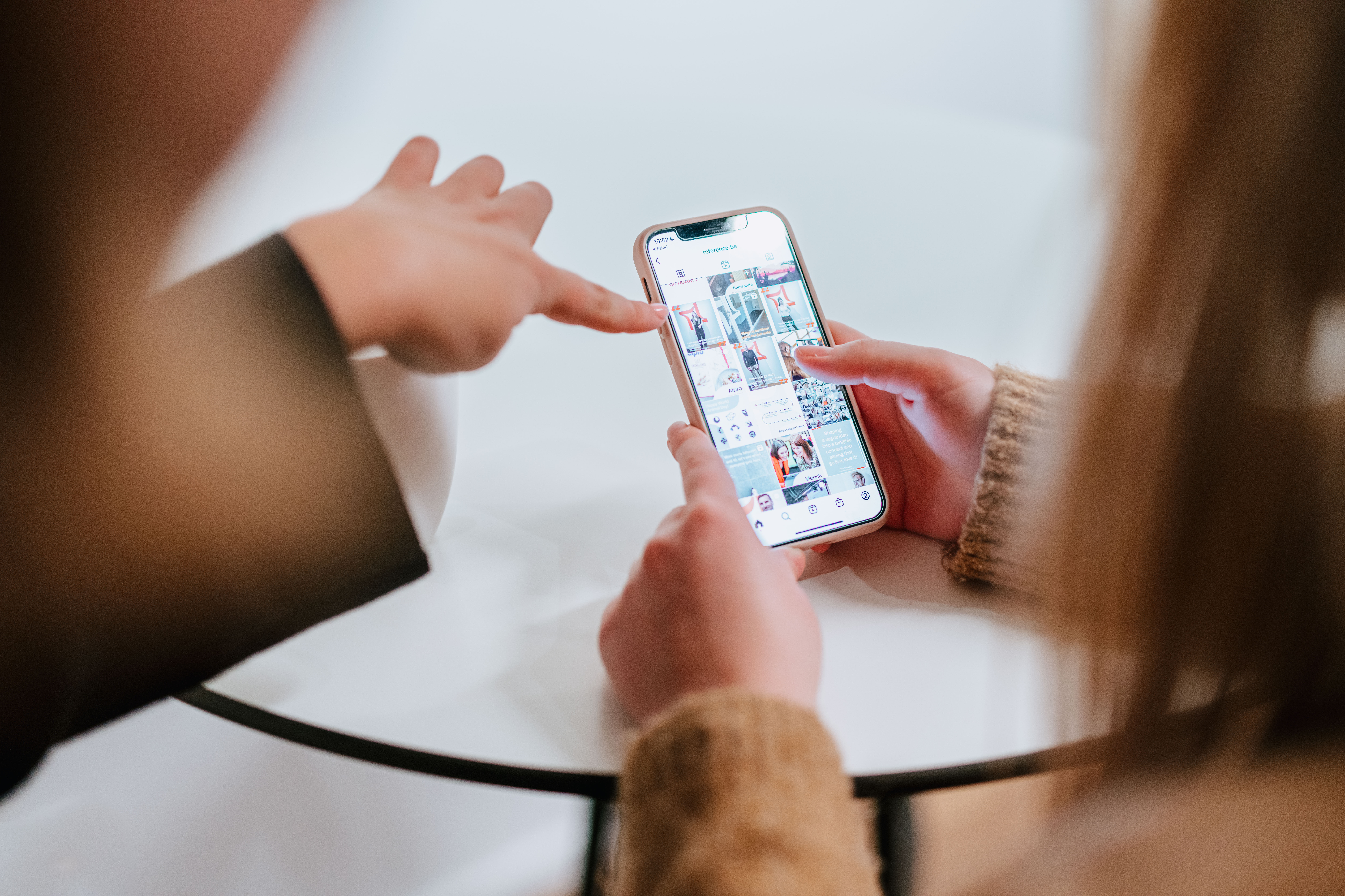 Focused shot of a mobile screen of the instagram account of The Reference with one person pointing at the screen