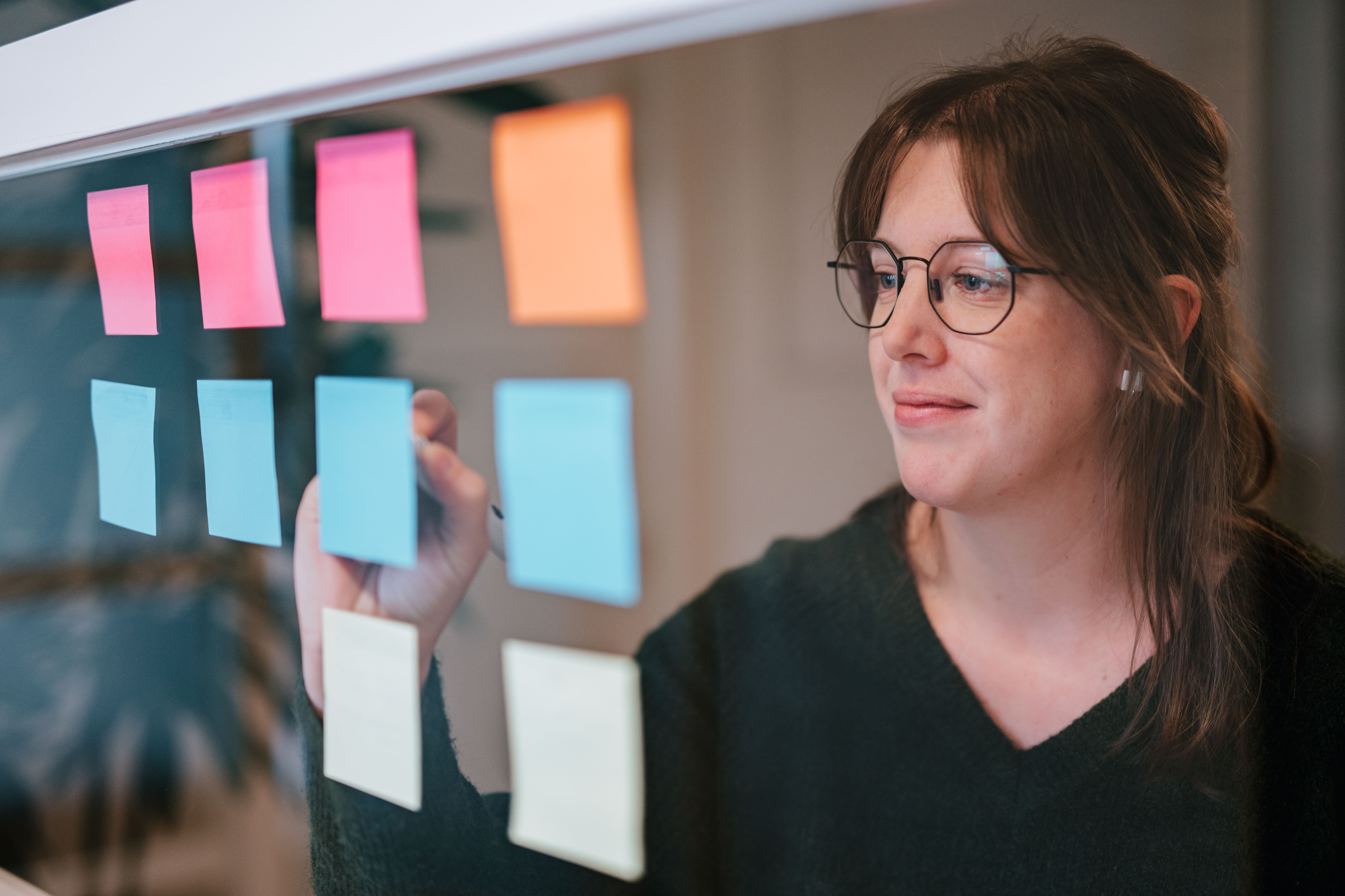 Focused shot of person writing on a post-it hanging on a glass wall