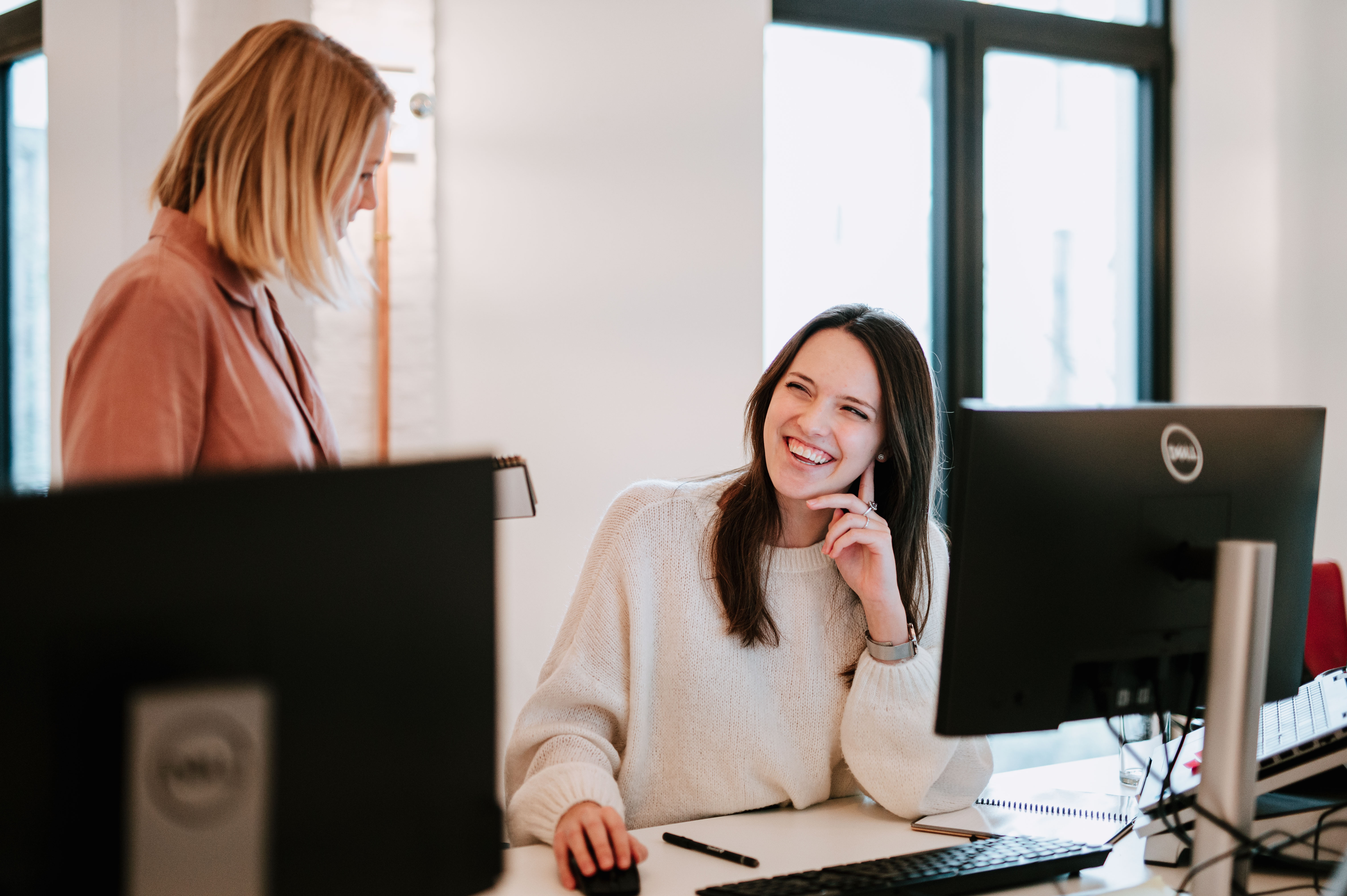 Two people in conversation, laughing, sitting at a desk