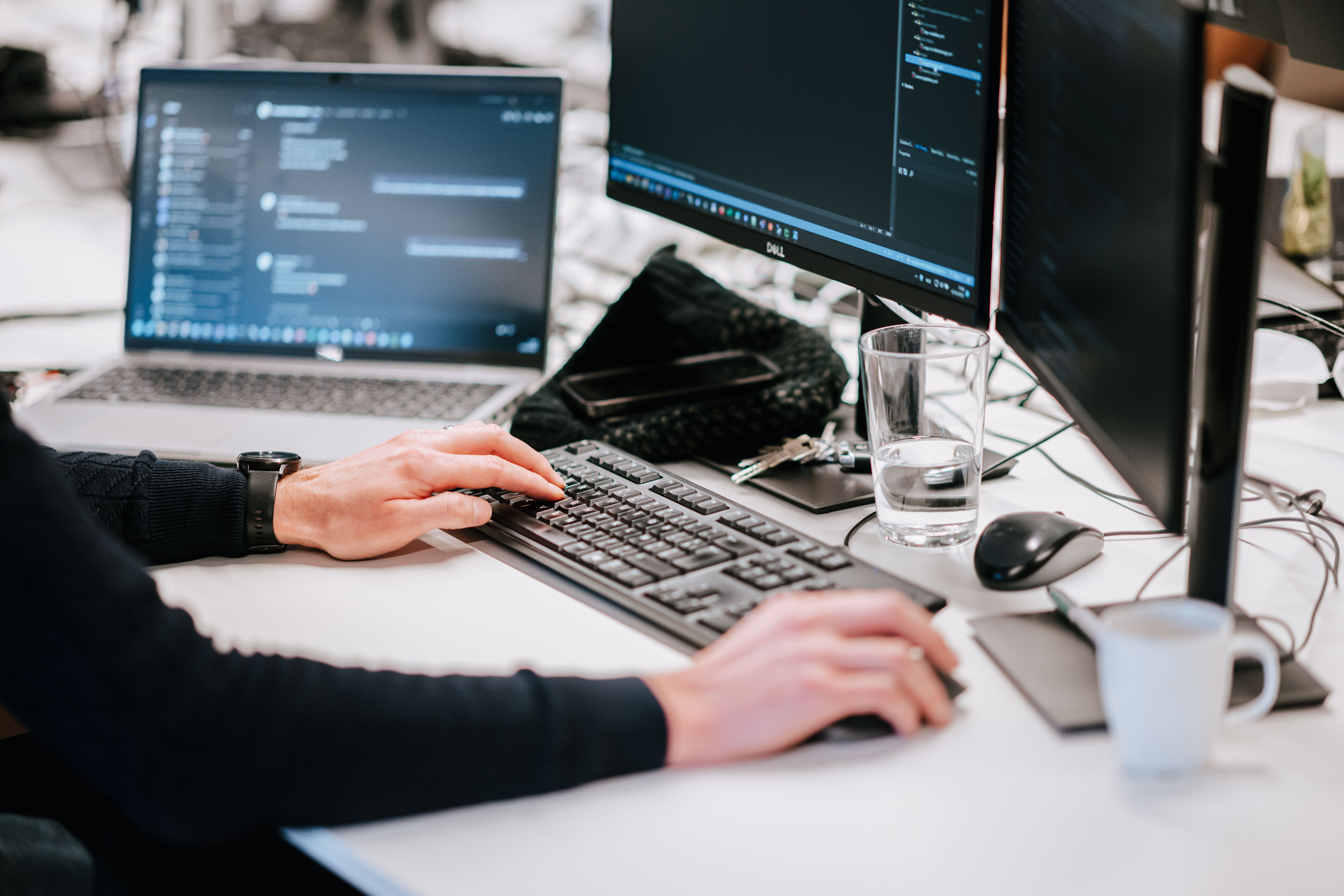 A desk with three screens and the hands of a person on the keyboard